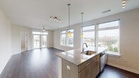 Located at 516 Rigsbee Ave in downtown Durham, NC, this single-floor unit offers a contemporary open-concept design that seamlessly connects the living, dining, and kitchen areas. Rich, dark hardwood flooring runs throughout the main living spaces, complemented by neutral walls and abundant natural light streaming through an expansive bank of large windows that frame impressive views of the Durham skyline. A ceiling fan with a brushed gold finish adds a refined touch to the living area, while French doors open onto a private balcony, further enhancing the connection to the surrounding urban landscape.

The kitchen is thoughtfully appointed with granite countertops, a large central island featuring an undermount sink, warm wood-toned cabinetry, stainless steel appliances, and a tile backsplash. Pendant lights and a track lighting system illuminate the space effectively. The bathroom includes a soaking tub with tile surround, a separate glass-enclosed shower, dual granite-topped vanity with ample cabinetry, and tile flooring. Bedroom spaces feature plush carpet, generous windows with city views, and well-sized closets with wire shelving. Overall, the unit presents a clean, modern aesthetic well-suited to urban living.