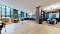 Located at 1900 S Hanover St in Baltimore's vibrant South Baltimore neighborhood, this expansive single-floor amenity lounge spans over 3,000 square feet of thoughtfully designed communal space. The interior is anchored by wide-plank light oak hardwood flooring laid in a herringbone pattern, which flows seamlessly throughout the entire floor plan, lending warmth and visual continuity.

The main lounge area is defined by a striking coffered ceiling with dark wood beams, adding architectural depth and a refined character. Large floor-to-ceiling windows flood the space with natural light and provide views of the surrounding neighborhood. A curated lounge corner features a plush sectional sofa, wall-mounted artwork, and elegant sconce lighting.

A sleek bar area serves as a central hub, complete with a dark island, bar seating, pendant lighting, and multiple mounted screens. Adjacent to the bar, a social lounge offers curved banquette seating and individual bistro tables, framed by deep green accent walls and built-in open shelving styled with decorative objects.

A private dining area features a long conference-style table beneath dramatic pendant fixtures, enclosed by dark-framed glass partitions. A game room with a billiards table and direct views to the outdoors adds a recreational dimension. The entry foyer is bright and welcoming, with glazed double doors opening to the exterior courtyard.