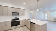 Located at 12608 E Nora Ave in Spokane Valley, WA, this well-appointed one-bedroom, one-bathroom unit offers a thoughtfully designed layout with modern finishes throughout. The open-concept kitchen and living area serves as the heart of the space, featuring light wood-tone cabinetry, crisp white quartz countertops, a peninsula with an integrated sink, and a full suite of stainless steel appliances including a refrigerator, electric range, microwave, and dishwasher. Pendant lighting above the peninsula adds a contemporary touch, while recessed ceiling lights brighten the entire area. Light wood-look plank flooring flows through the main living and kitchen areas, contributing to a clean and cohesive aesthetic. The living room offers access to an exterior door, bringing in natural light and outdoor views. The bedroom is carpeted for comfort and features a window with exterior views, providing a quiet and private retreat, along with access to a dedicated closet. The bathroom is finished with a light wood vanity, white quartz countertop, a tub-shower combination, and matching plank flooring, maintaining the unit's consistent modern palette. Neutral wall tones and recessed lighting throughout create a bright, inviting ambiance.