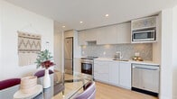 This well-designed one-bedroom, one-bathroom unit in Surrey, BC offers a thoughtful layout that maximizes every inch of its compact footprint. Light hardwood flooring runs throughout, tying the spaces together with a clean, cohesive aesthetic. The open-concept kitchen is a functional highlight, featuring flat-panel cabinetry in a soft grey tone, a decorative mosaic tile backsplash, stainless steel appliances including a full-size refrigerator, electric range, built-in microwave, and dishwasher, all complemented by light countertops. A glass-top dining table adjacent to the kitchen makes efficient use of the living area. A long entry corridor leads toward the living space, which is anchored by expansive floor-to-ceiling windows that frame sweeping panoramic views and flood the interior with natural light. The bedroom is a serene retreat, featuring a large window with elevated city and sky views, soft neutral tones, and a sliding-door closet offering ample storage. The bathroom is clean and modern, with tile flooring, a soaker tub-shower combination with full tile surround, and a floating white vanity with an integrated sink. Recessed lighting throughout maintains a bright, contemporary atmosphere.