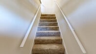 Located at 4441 E Honeygrove Ct in Virginia Beach, Virginia, this two-story home offers a well-organized layout across two levels. The main floor serves as the heart of the home, featuring a combined dining and living area with neutral carpet flooring and a textured ceiling that adds subtle visual character. Adjacent to the living space is a dedicated kitchen with hardwood-style flooring and a stainless steel refrigerator, connected via an open doorway for ease of flow. A laundry area and multiple closets—five in total—provide generous storage throughout. The bathroom on the main level is outfitted with a full tub-and-shower combination accented by brushed nickel grab bars, tile surround, and hardwood-style flooring. Carpeted staircases with white-painted railings connect the two levels. The upper level hosts the spacious primary bedroom, featuring soft carpet, a double-door closet, and multiple windows that invite natural light and outdoor views of the surrounding neighborhood. Additional rooms on the upper floor offer flexibility and feature the same warm, neutral palette with carpet and natural light. The home's clean, light-toned walls and consistent finishes throughout create a bright and cohesive living environment.