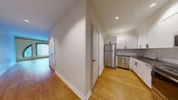 Located at 2 Broad St in Boston's historic Financial District, this one-bedroom, one-bathroom residence offers a thoughtfully designed layout across a single floor. Warm hardwood flooring flows consistently throughout the space, creating a cohesive and inviting atmosphere.

The open living area is a standout, anchored by a dramatic arched window that frames views of the surrounding historic brick streetscape and floods the room with natural light. Recessed lighting complements the natural illumination throughout.

The kitchen is outfitted with white shaker-style cabinetry, a classic subway tile backsplash, stainless steel appliances including a full-size refrigerator and dishwasher, and ample counter space — delivering both style and functionality.

The bedroom is a well-proportioned private retreat featuring hardwood floors, a standard window with exterior views, and dual built-in closets providing generous storage. A hallway connects the main living areas efficiently.

The bathroom is clean and modern, featuring large-format floor tiles, white subway tile surrounding a soaking tub with an overhead shower, a white vanity with a dark countertop, and chrome fixtures — presenting a crisp, contemporary aesthetic throughout.