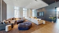 Located at 501 Brazos St in the heart of downtown Austin, Texas, this contemporary amenity space delivers a refined, upscale atmosphere across a single, generously proportioned floor. The design aesthetic is distinctly modern, characterized by textured dark wood-paneled accent walls, large-format tile flooring, and a striated metal ceiling that adds industrial sophistication throughout.

Two distinct living areas define the layout. The primary lounge is a grand, open volume anchored by expansive floor-to-ceiling windows that flood the space with natural light and offer views of the surrounding Austin skyline. Deep, neutral-toned sectional sofas, plush area rugs, and sculptural ottomans create a welcoming and social atmosphere. A large wall-mounted display serves as a focal point. A second, more intimate seating area mirrors this refined sensibility with curated furnishings and an additional mounted screen.

A dedicated meeting and dining area features herringbone-patterned flooring, a communal wood table with stylish seating, and a bold teal accent wall, accessible via glass sliding doors that provide visual connectivity while maintaining acoustic separation. A smaller workspace nook with sheer-draped windows offers a quiet retreat. A connecting hallway with glazed entry doors ties the zones together seamlessly, reinforcing the cohesive, hotel-caliber design throughout.
