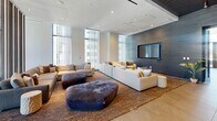 Located at 501 Brazos St in the heart of downtown Austin, Texas, this contemporary amenity space delivers a refined, upscale atmosphere across a single, generously proportioned floor. The design aesthetic is distinctly modern, characterized by textured dark wood-paneled accent walls, large-format tile flooring, and a striated metal ceiling that adds industrial sophistication throughout.

Two distinct living areas define the layout. The primary lounge is a grand, open volume anchored by expansive floor-to-ceiling windows that flood the space with natural light and offer views of the surrounding Austin skyline. Deep, neutral-toned sectional sofas, plush area rugs, and sculptural ottomans create a welcoming and social atmosphere. A large wall-mounted display serves as a focal point. A second, more intimate seating area mirrors this refined sensibility with curated furnishings and an additional mounted screen.

A dedicated meeting and dining area features herringbone-patterned flooring, a communal wood table with stylish seating, and a bold teal accent wall, accessible via glass sliding doors that provide visual connectivity while maintaining acoustic separation. A smaller workspace nook with sheer-draped windows offers a quiet retreat. A connecting hallway with glazed entry doors ties the zones together seamlessly, reinforcing the cohesive, hotel-caliber design throughout.