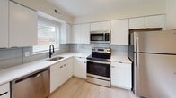Located at 150 S Bridge St in Somerville, NJ, this single-floor, one-bedroom, one-bathroom residence offers a clean, modern aesthetic throughout. Light wood-style flooring runs seamlessly across the living spaces, lending a bright and cohesive feel to the interior. The open living area is well-lit by multiple windows dressed with white blinds, allowing ample natural light to fill the space. A sliding glass door opens directly to a grassy outdoor area, providing convenient outdoor access and pleasant views. The contemporary kitchen is outfitted with sleek white flat-panel cabinetry extending to the ceiling, a light-toned countertop, a tile backsplash, a stainless steel sink with a matte black faucet, and a full suite of stainless steel appliances including a refrigerator, electric range, over-the-range microwave, and dishwasher. The bedroom is a generously proportioned room featuring dual windows for natural light and neutral wall tones that create a calm, restful atmosphere. The bathroom is finished with large-format light gray wall tiles, a soaking tub with an overhead rain showerhead, and matte black fixtures that add a sophisticated contrast. The overall design palette—white, light gray, and warm beige—creates a fresh, contemporary living environment throughout.