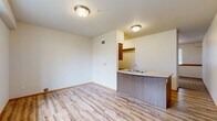Located at Water Lily Loop in Bellingham, Washington, this efficiently designed single-floor unit offers a thoughtful layout that maximizes its compact footprint. The space features warm wood-look vinyl plank flooring throughout the main living and kitchen areas, creating a cohesive and inviting aesthetic.

The kitchen is a standout feature, anchored by a curved peninsula with stone-look countertops and a double-basin sink. Medium-toned wood cabinetry lines the walls alongside stainless steel appliances, including a gas range, microwave, and refrigerator. A dishwasher is integrated beneath the peninsula, adding everyday convenience.

The bedroom area is carpeted for comfort and includes a closet along with a sliding barn-style door that opens into one of the two bathrooms. This en-suite bathroom features warm wood cabinetry, a vanity mirror with overhead lighting, and wood-look flooring. The second bathroom is clean and functional, finished in white with a soaking tub-shower combination, a towel bar, and wood-look flooring. Neutral white walls throughout the unit contribute to a bright, open feel.