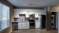 Located on 9th Street in Durham, NC, this single-floor space offers a clean, modern aesthetic throughout. The kitchen is a standout feature, designed with efficiency and style in mind. Crisp white cabinetry extends floor-to-ceiling, maximizing storage while contributing to a bright, open feel. Granite countertops provide durable, attractive work surfaces, complemented by a neutral gray subway tile backsplash that adds texture without overwhelming the space. A full suite of stainless steel appliances — including a refrigerator, electric range, built-in microwave, and dishwasher — gives the kitchen a polished, contemporary look. Track lighting mounted on the ceiling ensures the workspace is well-lit. The warm-toned hardwood-style flooring runs throughout, adding continuity and a welcoming contrast to the otherwise cool, modern palette. The overall design is cohesive and functional, reflecting a thoughtfully curated interior that balances practicality with contemporary urban style. This space is well-suited for those seeking a move-in-ready home in the heart of Durham's vibrant 9th Street corridor.