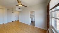 Located in the heart of Hollywood at 6500 Yucca St, Los Angeles, this single-floor unit combines industrial character with modern updates for a distinctive living experience. The main living area is generously proportioned, featuring warm light hardwood flooring throughout, crisp white walls, and a ceiling fan that adds both style and functionality. A standout feature of the space is the exposed red brick wall, which adds rich texture and industrial charm, framed by large windows that invite natural light and offer views of the surrounding Hollywood neighborhood, including glimpses of palm trees and nearby architecture. The open layout flows seamlessly from the living area into the kitchen, which is accessed through a dedicated opening. The kitchen is outfitted with white shaker-style cabinetry, light countertops, a stainless steel sink with a modern faucet, and tile flooring — offering a clean, contemporary aesthetic. The bathroom is finished with a tiled tub and shower combination, maintaining the unit's clean and functional design language. Overhead HVAC venting is integrated into the ceiling alongside flush-mount lighting, ensuring year-round comfort. The overall ambiance is bright, airy, and urban, blending classic architectural details with updated finishes throughout.