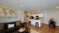 This single-floor residence offers a thoughtfully designed open-concept layout that seamlessly connects the living, dining, and kitchen areas. The living room is bright and welcoming, featuring a wall-mounted mini-split climate system, sliding glass doors that allow abundant natural light, and crown molding that adds a refined architectural touch.

The kitchen is a standout feature, showcasing white shaker cabinetry extending to the ceiling, a teal subway tile backsplash, stainless steel appliances including a refrigerator, range, and built-in microwave, and a spacious white quartz peninsula with an undermount sink and bar seating — ideal for casual dining or entertaining.

Warm hardwood-style flooring runs throughout the unit, creating a cohesive and inviting atmosphere. A hallway connects the main living area to two well-sized bedrooms. The primary bedroom includes a mirrored sliding-door closet, while a secondary bedroom offers a wall-mounted climate unit and a serene, neutral palette. The primary bathroom features a dual-sink white vanity, wood-framed mirrors, and a tiled walk-in shower. A second full bathroom with a white vanity and hardwood-style flooring provides additional convenience. Recessed lighting and crown molding are consistent throughout, lending the space a clean, polished character.