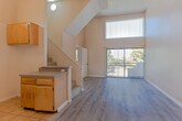 Located at 10500 Sherman Grove Ave in the Sunland-Tujunga neighborhood of Los Angeles, CA, this two-story residence offers a well-organized layout with functional living spaces across both levels. The main living area immediately impresses with its dramatic vaulted ceiling that rises across both floors, creating an open and airy atmosphere. Hardwood-style flooring runs throughout the living area, while a large sliding glass door fitted with vertical blinds invites natural light and provides views of the surrounding greenery. A carpeted staircase with a railing leads to the upper level, which features an open landing overlooking the main floor below. The kitchen is efficiently designed with warm wood cabinetry, granite-style countertops, a double-basin sink, tile flooring, and ample upper and lower storage. The bathroom includes a full shower-tub combo with clean white surrounds, tile flooring, and classic fixtures. The bedroom is generously sized with plush carpet, warm neutral-toned walls, a textured ceiling, a closet, and a window that allows natural light to filter in, alongside a connected bathroom. Throughout the home, textured ceilings and warm earth-tone walls contribute to a cohesive and comfortable aesthetic.