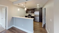Located at 7800 Westside in San Diego, Unit #212 is a thoughtfully designed single-floor residence that blends modern finishes with comfortable, functional living spaces. The open-concept layout is anchored by a stylish kitchen featuring dark espresso cabinetry, white countertops, stainless steel appliances including a gas range, microwave, and refrigerator, and pendant lighting that adds warmth over the peninsula breakfast bar. Rich wood-look flooring runs throughout the main living and dining areas, complementing the neutral wall tones and creating a cohesive, contemporary aesthetic. Large windows fitted with blinds allow generous natural light to fill the living area, which also benefits from track lighting overhead. The bedroom areas are finished with plush carpeting and offer a calm, restful atmosphere, with one bedroom featuring a sliding glass door that opens directly onto a private balcony overlooking mature greenery. The bathrooms are clean and functional, each featuring a full tub-shower combination with chrome fixtures, white tile surrounds, and wood-look flooring. One bathroom includes a vanity with a white countertop and a well-lit mirror. The entry foyer provides a welcoming transition into the home. Overall, the unit offers a bright, move-in-ready environment with quality finishes throughout.