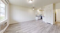 Located in the Jayhawks community of Rapid City, South Dakota, this single-floor unit offers a clean, modern layout designed for comfortable everyday living. Throughout the space, light gray luxury vinyl plank flooring provides a cohesive and low-maintenance foundation that complements the soft, neutral wall tones.

The open living area is bright and welcoming, with large windows that allow natural light to fill the room and provide views of the surrounding neighborhood. A wall-mounted HVAC unit ensures year-round climate control, and a dedicated electrical panel is conveniently accessible.

The galley-style kitchen is efficiently designed with ample white cabinetry, granite-style countertops, and a full suite of black appliances including a range, microwave, dishwasher, and refrigerator. A stainless steel sink and an exterior-facing door add both functionality and additional natural light to the kitchen.

The bedroom is a comfortable, well-proportioned space featuring a large window with outdoor views and an open closet for storage. The full bathroom includes a tub-shower combination, a toilet, and a vanity with granite-style countertops and white cabinetry. An in-unit water heater is also housed within the bathroom utility area. The overall design is clean and practical, making this a functional and move-in ready residence.
