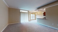 This single-floor residence features a thoughtfully designed open-concept layout connecting the living area and kitchen. The spacious living room is finished with plush carpeting, warm neutral-toned walls, and crown molding throughout. Large windows with vertical blinds allow ample natural light to fill the space, while a corner window arrangement adds architectural interest.

The kitchen is well-equipped with rich dark-stained cabinetry, dark granite countertops, stainless steel appliances including a gas range, microwave, and refrigerator, and recessed lighting overhead. A breakfast bar with elegant pendant lighting creates a natural boundary between the kitchen and living area, with tile flooring completing this space.

The bedroom includes plush carpeting, crown molding, a ceiling fan, and access to a walk-in closet with built-in shelving. An additional flexible room features built-in wall shelving, making it well-suited as a home office or den. The bathroom is finished with neutral ceramic tile surrounding the tub-shower combination, accented by a decorative mosaic tile border, complemented by tile flooring and brushed nickel fixtures.