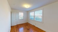 Located at 1000 Hill St in Greensboro, NC, this single-floor home offers a clean, straightforward layout with a consistent design language throughout. Warm-toned hardwood floors extend across the living areas and bedrooms, providing a classic and durable foundation that adds character to each room. Crisp white walls and trim create a bright, neutral backdrop throughout the interior.

The living area is welcoming and well-lit, benefiting from a window that frames views of the surrounding greenery. Multiple bedrooms are present, each featuring the same rich hardwood flooring and generous window arrangements fitted with blinds, allowing for excellent natural light and privacy control. The rooms feel open and airy, with clean lines and ample floor space.

The kitchen is functionally appointed with white cabinetry both above and below the countertops, a double-basin stainless steel sink, warm laminate countertops, and a window overlooking the outdoors. Tile flooring grounds the kitchen area and provides a practical contrast to the hardwood found elsewhere.

The bathroom is finished with white subway-style wall tile and includes a full tub and shower combination, a toilet, and a frosted window for natural light and privacy. Floor-level vents are present throughout the home, indicating a central HVAC system. Overall, the home presents a tidy, functional, and well-maintained living environment.