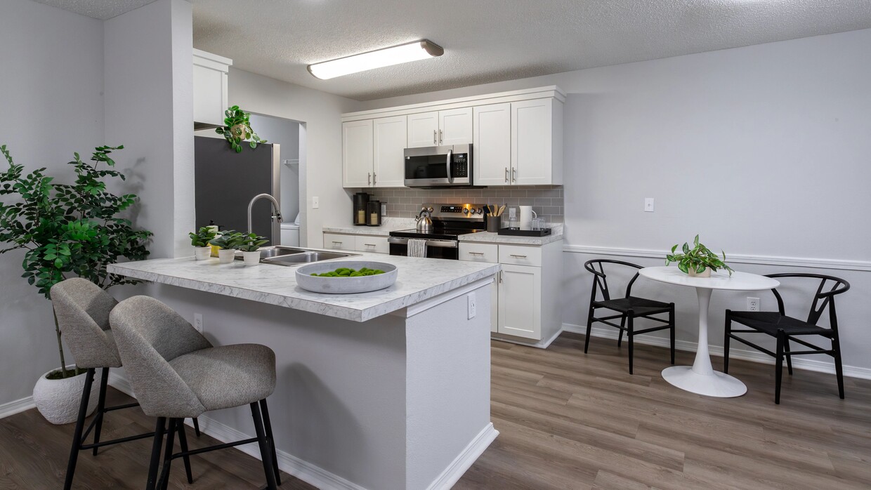 Enjoy the contemporary design of this kitchen featuring a breakfast bar, stainless steel appliances, and a comfortable dining area. - The Avenue