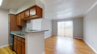 This single-floor, one-bedroom, one-bathroom residence offers a thoughtfully designed layout that maximizes functionality throughout. The open living area features light-toned hardwood flooring and neutral gray walls accented by crown molding, creating a clean and cohesive aesthetic. A sliding glass door floods the space with natural light and provides direct access to a private balcony, extending the living area outdoors.

The galley-style kitchen is efficiently arranged with warm wood cabinetry offering ample storage, granite-style countertops, and black appliances including a range, microwave, and refrigerator. A peninsula with a built-in sink separates the kitchen from the dining area, which is defined by a pendant light fixture overhead.

The bedroom provides a comfortable retreat with plush carpeting, neutral walls, and a window with blinds that allows for natural light. A walk-in closet adjacent to the room adds valuable storage capacity.

The bathroom features hardwood flooring, a wood vanity with a granite-style countertop, and a full tub-shower combination with white tile surround. Throughout the unit, consistent finishes and a neutral color palette create a cohesive and inviting atmosphere.