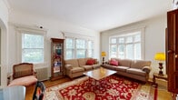 Located on West Ferry Street in Buffalo's historic Allentown neighborhood, this two-bedroom, one-bathroom residence showcases timeless architectural charm across a well-appointed single floor. The living room is a standout space, bathed in natural light through expansive leaded glass windows, with warm hardwood floors and classic radiator heating lending an inviting, period-appropriate character. The hallway features a striking dark-painted tray ceiling accented by a decorative chandelier, with wainscoting and an arched doorway adding architectural interest. The full bathroom continues the vintage aesthetic with a classic blue-and-white mosaic tile floor, subway tile walls with decorative border accents, a soaking tub, and an arched niche detail. The spacious primary bedroom offers bay windows with floral drapery and a chandelier overhead, while the second bedroom is a cozy, well-defined room with clean white walls. The dining room features two-tone painted walls, tile flooring, a pendant light fixture, and bright windows with a view. The kitchen includes warm oak cabinetry, tile flooring, and a window for natural light. Two hallways connect the rooms efficiently, completing this cohesive and character-rich residence.