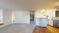 Located at 9455 SW 125th Ave in Beaverton, Oregon, this single-floor apartment offers two bedrooms and one bathroom across a well-organized layout. The living room serves as the heart of the home, highlighted by a classic fireplace with a white mantel and a charming bay window with built-in bench seating, allowing natural light to filter in and offering views of the surrounding greenery. The living area features neutral carpet and connects seamlessly to the entry, where hardwood flooring extends into the kitchen. The kitchen is efficiently designed with a wraparound peninsula, white cabinetry accented by warm wood-toned upper cabinets, laminate countertops, a ceiling fan, and hardwood flooring — providing both functionality and a bright, open feel. The primary bedroom is generously sized, featuring soft carpet, a large sliding-door closet, and an additional door providing convenient access. The second bedroom is a comfortable, carpeted room with good natural light. The full bathroom includes a vanity with under-sink storage, a framed mirror, and hardwood flooring. Throughout the unit, warm wood-toned door accents and neutral wall tones create a cohesive, understated aesthetic.