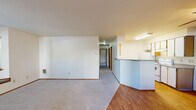 Located at 9455 SW 125th Ave in Beaverton, Oregon, this single-floor apartment offers two bedrooms and one bathroom across a well-organized layout. The living room serves as the heart of the home, highlighted by a classic fireplace with a white mantel and a charming bay window with built-in bench seating, allowing natural light to filter in and offering views of the surrounding greenery. The living area features neutral carpet and connects seamlessly to the entry, where hardwood flooring extends into the kitchen. The kitchen is efficiently designed with a wraparound peninsula, white cabinetry accented by warm wood-toned upper cabinets, laminate countertops, a ceiling fan, and hardwood flooring — providing both functionality and a bright, open feel. The primary bedroom is generously sized, featuring soft carpet, a large sliding-door closet, and an additional door providing convenient access. The second bedroom is a comfortable, carpeted room with good natural light. The full bathroom includes a vanity with under-sink storage, a framed mirror, and hardwood flooring. Throughout the unit, warm wood-toned door accents and neutral wall tones create a cohesive, understated aesthetic.