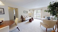 This single-floor residence offers a comfortable and thoughtfully designed layout that balances open communal spaces with private retreats. The living room serves as the heart of the home, bathed in natural light streaming through a large sliding glass door that opens onto a private balcony overlooking lush greenery. Plush wall-to-wall carpeting and neutral warm tones create a welcoming atmosphere throughout.

Adjacent to the living area, the dining space features a decorative niche built into the wall, pendant lighting overhead, and room for a full dining set — an ideal spot for meals and entertaining. The kitchen is outfitted with warm wood cabinetry, ample counter space, a stainless steel sink, and includes a dishwasher, offering practical functionality in a compact footprint.

The residence includes two bedrooms, each carpeted and filled with natural light from well-dressed windows. The primary bedroom is generously sized to accommodate a king bed and additional furnishings, while the secondary bedroom offers a cozy, versatile space with closet storage. A full bathroom features a classic tiled tub-shower combination in a clean, bright finish.

Throughout the space, a cohesive neutral palette and open sightlines contribute to an airy, relaxed ambiance well-suited for everyday living.