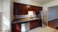 This single-floor residence offers a thoughtfully designed layout that balances comfort and functionality. The kitchen is a standout feature, showcasing rich dark-wood cabinetry with shaker-style doors, granite-look countertops, a stone tile backsplash, and a full suite of stainless steel appliances including a range, microwave, dishwasher, and refrigerator. A window above the sink brings in natural light, brightening the space throughout the day.

The bathroom is elegantly appointed with large-format tile flooring, a tiled tub-and-shower combination with a decorative mosaic accent border, a dark-wood vanity with an undermount sink, and a bright window that adds an airy feel to the room.

The living area features warm, rich hardwood flooring and neutral walls, creating an inviting and versatile space. A large window frames views of lush greenery outside. The bedrooms are finished with plush carpeting and feature multiple windows that flood the rooms with natural light and offer pleasant outdoor views. The layout, as seen in the dollhouse view, flows efficiently between the kitchen, living spaces, bathroom, and bedrooms, making excellent use of the available footprint.