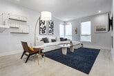 Located in the heart of Los Angeles, this single-floor residence at 5955 Saturn St blends contemporary design with elevated city living. The open-concept layout connects a well-appointed kitchen, casual living area, and formal dining space, creating a seamless flow throughout. The kitchen features light wood cabinetry, white quartz countertops, stainless steel appliances including a gas range, and a peninsula that opens to the living area — ideal for entertaining. The dining area is anchored by a sculptural pendant light cluster and a large black-framed window offering sweeping panoramic views of the Los Angeles skyline. The living room is bright and airy, with multiple windows framing treetop and city views, recessed lighting, and light hardwood flooring. Each bedroom is thoughtfully designed with plush carpeting, generous closet space, and large windows that bring in abundant natural light and expansive views of the surrounding cityscape. The primary bedroom features a wall of windows with direct views toward downtown LA, complemented by clean, neutral finishes. A well-finished bathroom includes a tiled tub-shower combination and modern vanity. Crisp white walls and soft grey tones throughout lend the space a calm, cohesive ambiance.