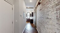 Located at 1821 E Hagert St in Philadelphia's vibrant Fishtown neighborhood, this one-bedroom, one-bathroom unit masterfully blends historic industrial character with modern updates. Exposed brick walls, original hardwood floors, and soaring ceilings with rustic wooden beams define the space's raw, loft-inspired aesthetic throughout.

The open combined living and dining area is a standout, anchored by multiple large arched windows with black frames that flood the room with natural light and offer views of the surrounding neighborhood. The exposed brick accent wall and a distinctive industrial barn-style sliding door add authentic character.

The kitchen is well-appointed with rich dark cabinetry, white countertops, stainless steel appliances including a refrigerator, electric range, microwave, and dishwasher, plus an arched window above the sink. Hardwood floors continue seamlessly into this space.

The bedroom features soaring ceilings, hardwood floors, and an arched window set into an exposed brick wall, creating a bright and characterful retreat. A dedicated closet provides storage. The bathroom is clean and functional, finished with large-format tile flooring and accessibility grab bars. Additional utility and laundry rooms complete the layout, offering practical convenience within this uniquely designed urban space.