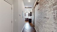 Located at 1821 E Hagert St in Philadelphia's vibrant Fishtown neighborhood, this one-bedroom, one-bathroom unit masterfully blends historic industrial character with modern updates. Exposed brick walls, original hardwood floors, and soaring ceilings with rustic wooden beams define the space's raw, loft-inspired aesthetic throughout.

The open combined living and dining area is a standout, anchored by multiple large arched windows with black frames that flood the room with natural light and offer views of the surrounding neighborhood. The exposed brick accent wall and a distinctive industrial barn-style sliding door add authentic character.

The kitchen is well-appointed with rich dark cabinetry, white countertops, stainless steel appliances including a refrigerator, electric range, microwave, and dishwasher, plus an arched window above the sink. Hardwood floors continue seamlessly into this space.

The bedroom features soaring ceilings, hardwood floors, and an arched window set into an exposed brick wall, creating a bright and characterful retreat. A dedicated closet provides storage. The bathroom is clean and functional, finished with large-format tile flooring and accessibility grab bars. Additional utility and laundry rooms complete the layout, offering practical convenience within this uniquely designed urban space.