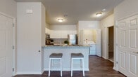 This single-story residence offers a well-organized, open-concept layout designed for comfortable everyday living. The kitchen serves as a central hub, outfitted with white cabinetry extending to the ceiling, granite-look countertops, and a full suite of stainless steel appliances including a refrigerator, gas range, and microwave. A peninsula with seating for two provides a casual dining option and naturally connects the kitchen to the living area. Immediately adjacent, a dedicated in-unit laundry alcove houses a full-size washer and dryer, adding a layer of convenience rarely found in similarly scaled residences. Rich, dark-toned hardwood-style flooring runs throughout the main living areas, adding warmth and visual continuity.

The living room is bright and welcoming, benefiting from a sliding glass door fitted with vertical blinds that invite natural light. The bedroom offers plush carpeting underfoot and a window with outdoor views, creating a calm, restful retreat. The bathroom features white cabinetry with under-sink storage, a single vanity with a wide mirror, and a tub-shower combination. Neutral wall tones throughout lend a clean, cohesive aesthetic across the entire space.