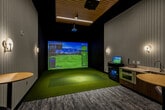This 360 square foot space in Seattle combines functionality with contemporary design. The single-floor layout comprises a hallway, a patio, and a versatile multi-purpose room. The hallway features sleek tile flooring and white walls, creating a bright, welcoming entrance. A standout feature is the expansive floor-to-ceiling windows that flood the space with natural light, offering views of the surrounding urban landscape.

The versatile room serves multiple functions. One section houses a state-of-the-art golf simulator with a large projection screen and green carpeting, perfect for entertainment or practice. Adjacent to this is a modern lounge area with comfortable seating, including stylish orange chairs and a round coffee table. The lounge is anchored by a patterned area rug that adds warmth to the polished concrete floors.

A glass-enclosed patio area serves as a transition between indoor and outdoor spaces, featuring wooden accents and additional seating. This area is ideal for relaxation or casual meetings. Throughout the space, pendant lighting and recessed fixtures provide ample illumination, complementing the abundant natural light. The overall design aesthetic is clean and minimalist, with a thoughtful blend of textures and materials that create a sophisticated, multi-functional environment.