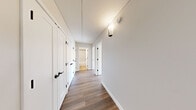 Located at 71 Village Way in Brookline, MA, this two-bedroom, one-bathroom residence offers a clean, modern aesthetic across a single thoughtfully arranged floor. Warm hardwood-style flooring runs throughout the entire space, creating a cohesive and inviting atmosphere from room to room.

The open living area connects seamlessly to a compact kitchen outfitted with white cabinetry and a built-in sink, forming an efficient and functional common space bathed in natural light. Neutral tones on the walls complement the light flooring, lending the area a bright and airy feel.

The spacious primary bedroom is generously sized, featuring dual closets with built-in shelving and organization systems, large windows that invite natural light and outdoor views of the surrounding neighborhood. The second bedroom is also well-proportioned, with its own window offering additional natural light.

A well-lit hallway, accented with a wall sconce and lined with multiple white-paneled doors with black hardware, connects all rooms in an efficient corridor. The bathroom is finished with a white countertop vanity, an under-mount sink, matte black fixtures, and a backlit mirror, offering a clean and contemporary look.

This residence combines practical layout design with modern finishes, making it a well-appointed home in the desirable Brookline area.