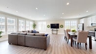 Located at 180 Westfall Town Dr in Matamoras, PA, this well-appointed single-floor community space offers a thoughtfully designed layout that balances comfort and functionality. The open-concept living and dining area serves as the heart of the space, featuring light hardwood-style flooring, crown molding, and recessed lighting throughout. Large multi-pane windows line the walls, flooding the interior with generous natural light and providing views of the surrounding community.

The living area accommodates a substantial sectional sofa and is anchored by a wall-mounted flat-screen TV framed by decorative wreaths. Adjacent to the living space, a formal dining area features a dark wood table with upholstered seating for six, positioned near bright windows overlooking green outdoor space.

The kitchen is outfitted with crisp white cabinetry, granite countertops, and stainless steel appliances including a refrigerator, range, and microwave — providing full amenities for gatherings or events.

A sun-drenched lounge nook with wraparound windows offers a quieter retreat, while a dedicated game room includes a foosball table, wall-mounted TV, and seating, making it an ideal space for recreational activities. The overall ambiance is clean, modern, and welcoming throughout.
