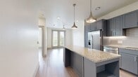 This contemporary 590 square foot apartment in Vitruvian West 2 offers a harmonious blend of style and functionality. The open-concept design seamlessly integrates the living room and kitchen, creating a spacious feel within the compact floor plan. The kitchen is a standout feature, boasting sleek gray cabinetry, granite countertops, and stainless steel appliances, complemented by stylish pendant lighting over a central island with built-in storage.

The bedroom, measuring 140 square feet, is bathed in natural light from large windows and features a modern ceiling fan. The bathroom continues the apartment's sophisticated aesthetic with a double vanity, granite countertops, and a glass-enclosed shower. Light wood-look flooring runs throughout the space, adding warmth and continuity.

French doors in the living area lead to a private balcony, offering outdoor space and views. The apartment's design maximizes natural light with multiple windows and high ceilings, enhancing the sense of spaciousness. Built-in closets provide ample storage solutions. This well-designed one-bedroom unit combines modern amenities with thoughtful layout, perfect for comfortable urban living.