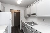 Located at 527 S 200 E in Salt Lake City, Utah, this 2-bedroom, 1-bathroom unit offers a well-organized floor plan across a single level. The spacious living room features plush wall-to-wall carpeting, a textured ceiling, and a large floor-to-ceiling window dressed with vertical blinds, framing expansive city views and filling the space with natural light. Track lighting runs along the ceiling, adding functional illumination throughout.

The galley-style kitchen is efficiently laid out with gray cabinetry, a white countertop, a full-size refrigerator, and wood-look flooring that extends underfoot. Light blue lower cabinets add a subtle pop of color and contrast against the neutral palette. A dishwasher is also included.

The generously sized primary bedroom offers plush carpet, a large closet with sliding panel doors, a wall-mounted HVAC unit, and its own window with city views. The second bedroom is comparably comfortable, also carpeted with closet access and track lighting.

The bathroom is clean and functional, featuring a full soaking tub with a handheld showerhead, grab bars for added safety, and neutral tile surrounds. A hallway connects the rooms, providing a logical flow throughout the unit. The textured ceilings are consistent across the space, lending a cohesive, classic character throughout.