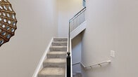 This three-floor townhome in Novi, Michigan offers a well-organized layout across its lower, main, and upper levels. The entry-level floor provides a practical transition space with access to the staircase connecting all three floors. Staircases feature neutral-toned carpet, dark-finished newel posts, and sleek metal baluster railings that add a contemporary touch throughout the vertical circulation.

The main level serves as the heart of the home, encompassing an open-concept living room, dining room, and kitchen. The living room stands out with dramatically high two-story ceilings, a ceiling fan, large windows that invite abundant natural light, and an upper-level overlook framed by iron railings. The kitchen features white cabinetry, stainless steel appliances, wood-look flooring, crown molding, and a sliding glass door opening onto a private balcony with tree-lined views. The adjacent dining area offers a bright window and crown molding detail.

The upper level houses three carpeted bedrooms, including a comfortably sized primary bedroom with large windows overlooking greenery. Two additional flexible office or den spaces, three full bathrooms — including one with a tub-shower combination — a utility room, and multiple hallways round out the functional layout of this multi-level home.