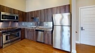 Located at 75 S Main St in Sharon, Massachusetts, this single-floor unit offers a well-designed layout with a cohesive blend of modern finishes and functional spaces. The open-concept living and dining area is anchored by warm hardwood flooring and neutral wall tones, with multiple large windows allowing generous natural light to fill the space. The kitchen features sleek dark walnut cabinetry, granite countertops, a stainless steel refrigerator, dishwasher, range, and microwave, all set against a clean tile backsplash. Recessed lighting and an open sightline to the living area make the kitchen both practical and visually connected to the rest of the home. The bedrooms are finished with plush carpeting and neutral walls, each offering natural light through well-positioned windows. One bedroom includes a walk-in closet outfitted with wire shelving and hanging rods for ample storage. Both full bathrooms are finished with light tile flooring, dark walnut vanity cabinetry, light countertops, and tub-shower combinations with chrome fixtures. A hallway connects the private areas of the unit, which also includes an electrical panel access point. The overall ambiance is clean, modern, and move-in ready.