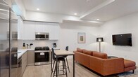 Located in the heart of Los Angeles at 626 N Wilton Place, this modern unit offers four bedrooms and four bathrooms across a single floor. The open-concept layout seamlessly connects the living area to the kitchen, creating a bright and functional shared space. The contemporary kitchen is equipped with stainless steel appliances — including a gas range, dishwasher, and microwave — complemented by two-tone cabinetry in white and warm gray, white quartz countertops, and a central dining table with bar-height seating. Light wood flooring runs throughout, enhancing the clean, cohesive aesthetic. The living room features a wall-mounted TV, recessed lighting, and a comfortable seating area. Each of the four bedrooms is well-proportioned with neutral walls and light flooring; one bedroom includes a window overlooking a shared courtyard, while the primary bedroom features closet space. The four bathrooms are finished in a minimalist style, each offering a full tub-shower combination with large-format white tile surround and clean chrome fixtures. A dedicated in-unit washer and dryer is conveniently accessible from the living area, adding everyday practicality to this well-appointed Los Angeles residence.