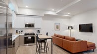 Located in the heart of Los Angeles at 626 N Wilton Place, this modern unit offers four bedrooms and four bathrooms across a single floor. The open-concept layout seamlessly connects the living area to the kitchen, creating a bright and functional shared space. The contemporary kitchen is equipped with stainless steel appliances — including a gas range, dishwasher, and microwave — complemented by two-tone cabinetry in white and warm gray, white quartz countertops, and a central dining table with bar-height seating. Light wood flooring runs throughout, enhancing the clean, cohesive aesthetic. The living room features a wall-mounted TV, recessed lighting, and a comfortable seating area. Each of the four bedrooms is well-proportioned with neutral walls and light flooring; one bedroom includes a window overlooking a shared courtyard, while the primary bedroom features closet space. The four bathrooms are finished in a minimalist style, each offering a full tub-shower combination with large-format white tile surround and clean chrome fixtures. A dedicated in-unit washer and dryer is conveniently accessible from the living area, adding everyday practicality to this well-appointed Los Angeles residence.