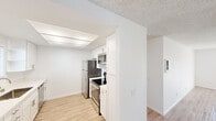 Located at 2636 Grand Ave in San Diego, CA, this single-floor unit offers a clean, modern aesthetic defined by bright white walls, light wood-style luxury vinyl flooring, and textured ceilings throughout. The open layout creates a sense of spaciousness, with natural light filtering in through multiple windows fitted with blinds.

The kitchen is well-appointed with white shaker-style cabinetry featuring brushed nickel hardware, white countertops, and a full suite of stainless steel appliances, including a refrigerator, electric range, built-in microwave, and dishwasher. Recessed panel lighting illuminates the kitchen area effectively.

The living areas are generously sized and open, with a structural column adding an architectural element to the floor plan. One room features a ceiling fan with an integrated light fixture, adding both comfort and functionality. Windows in the living and sleeping areas invite natural light and views of the surrounding neighborhood.

The bathroom is finished in a crisp, clean style with white surfaces, light wood-style flooring, a tub/shower combination with a curved curtain rod, a white vanity with brushed nickel hardware, and a full-width mirror. The overall ambiance of this San Diego residence is bright, fresh, and move-in ready.
