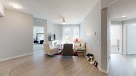 This single-floor residence offers a thoughtfully designed layout that balances comfort and contemporary style. The open-concept living area features light wood-style flooring, a ceiling fan, and large sliding glass doors fitted with vertical blinds that allow generous natural light and outdoor views. The space flows seamlessly into a dedicated dining area, highlighted by a pendant light fixture, a decorative mirror accent, and ample room for a full-size dining table. The kitchen is well-equipped with dark wood cabinetry, granite countertops, a classic white subway tile backsplash, stainless steel appliances including a dishwasher, a built-in wine rack, and a breakfast bar for casual dining. A conveniently placed in-unit laundry area is accessible directly from the kitchen. The primary bedroom is carpeted and generously sized, featuring a window that fills the room with natural light, and connects to an en-suite bathroom with dual sinks, a wide vanity with white cabinetry, and wood-look flooring. The second bedroom is equally comfortable, with plush carpeting, a large window, and neutral tones. A second full bathroom offers a soaking tub with shower combination, an extended vanity with ample storage, and wood-look tile flooring. Throughout the residence, soft gray walls and clean white trim contribute to a cohesive, modern aesthetic.