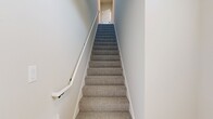 Located at 930 Terrapin Lane, Unit 203 in De Forest, WI, this 2-bedroom, 2-bathroom condo spans 1,250 square feet across two floors. The ground floor houses a spacious attached garage with an automatic opener and a concrete floor. The main living level on the upper floor encompasses 1,150 square feet and features light hardwood flooring throughout common areas. The open-concept kitchen and living room is a standout, boasting white shaker upper cabinets, gray lower cabinets, white quartz countertops, stainless steel appliances, a large center island with pendant lighting, and a black hardware accent throughout. The living area opens to a private balcony through sliding glass doors, offering scenic outdoor views. The primary bedroom measures 170 square feet with plush carpeting, a ceiling fan, and natural light from windows. Each bathroom features gray vanity cabinetry with white countertops and hardwood-style flooring. Both closets include wire shelving systems. A staircase connects the garage level to the main living floor. The unit's neutral palette, modern fixtures, and blend of hardwood and carpet flooring create a clean, contemporary ambiance throughout.
