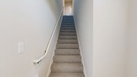 Located at 930 Terrapin Lane, Unit 203 in De Forest, WI, this 2-bedroom, 2-bathroom condo spans 1,250 square feet across two floors. The ground floor houses a spacious attached garage with an automatic opener and a concrete floor. The main living level on the upper floor encompasses 1,150 square feet and features light hardwood flooring throughout common areas. The open-concept kitchen and living room is a standout, boasting white shaker upper cabinets, gray lower cabinets, white quartz countertops, stainless steel appliances, a large center island with pendant lighting, and a black hardware accent throughout. The living area opens to a private balcony through sliding glass doors, offering scenic outdoor views. The primary bedroom measures 170 square feet with plush carpeting, a ceiling fan, and natural light from windows. Each bathroom features gray vanity cabinetry with white countertops and hardwood-style flooring. Both closets include wire shelving systems. A staircase connects the garage level to the main living floor. The unit's neutral palette, modern fixtures, and blend of hardwood and carpet flooring create a clean, contemporary ambiance throughout.