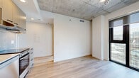 Located at 75 Slater Street in the heart of Ottawa, this one-bedroom, one-bathroom unit offers a thoughtfully designed layout that maximizes its compact footprint. The space features a cohesive modern aesthetic throughout, highlighted by light-toned hardwood flooring and crisp white walls that create a clean, airy atmosphere.

A standout architectural element is the exposed concrete ceiling, lending an industrial character that contrasts beautifully with the warm flooring and bright interiors. The living area benefits from dramatic floor-to-ceiling windows framed in sleek black, flooding the space with natural light and offering elevated views of the surrounding Ottawa cityscape.

The kitchen is well-appointed with contemporary cabinetry, a marble-effect backsplash, a stainless steel dishwasher, electric range, and an integrated refrigerator — all compactly arranged for efficient use of space. A wood-accented cabinet panel adds warmth to the kitchen's modern palette.

The bedroom is served by a dedicated closet and shares access to a bright hallway that connects all rooms efficiently. The bathroom is elegantly finished with large-format marble-style wall tiles, a soaking tub, and matte black fixtures including a rain showerhead and faucet, delivering a spa-like aesthetic. The hallway, illuminated by recessed lighting, leads naturally through the unit, completing a practical and polished one-floor layout.