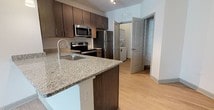 Located at 100 Whitworth Way in Williamsburg, Virginia, this single-floor residence offers a well-designed layout with a clean, modern aesthetic throughout. The kitchen is a standout feature, showcasing dark espresso cabinetry, granite countertops, and a full suite of stainless steel appliances including a range, microwave, refrigerator, and dishwasher. Light wood-style flooring runs through the kitchen and living areas, complemented by pendant lighting and a peninsula with an undermount sink that opens to the living space — ideal for everyday functionality and entertaining. The open-concept living area is bright and airy, with neutral white walls and ample room to customize. The bedrooms are generously proportioned, each finished with plush wall-to-wall carpet and ceiling fans for year-round comfort. The primary bedroom includes access to a dedicated bathroom and a walk-in closet, providing excellent storage. A secondary bedroom benefits from natural light through a window with blinds. The bathroom is outfitted with a full tub-shower combination featuring white tile surround and wood-style flooring. Throughout the space, consistent finishes and a neutral palette create a cohesive, move-in-ready environment suited for a variety of lifestyles.