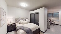This thoughtfully designed single-floor unit showcases a clean, contemporary aesthetic throughout, with neutral tones, light flooring, and dark accent finishes creating a cohesive and sophisticated atmosphere. The bedroom is comfortably proportioned, featuring a built-in sliding double closet with dark-framed doors, a flush ceiling light fixture, and soft, neutral walls that lend a calm and restful ambiance. The living area extends naturally from the bedroom and includes a wall-mounted ductless mini-split HVAC unit for year-round climate control, as well as a media console with an integrated electric fireplace, adding warmth and a stylish focal point to the room. The kitchen is efficiently laid out with rich, dark espresso-toned cabinetry reaching toward the ceiling, white quartz countertops, and a full suite of stainless steel appliances including a refrigerator, dishwasher, electric or gas range, and over-the-range microwave. A single-basin sink and tile backsplash complete the functional yet polished kitchen design. The bathroom is accessed through a sleek dark-framed door and features dark vanity cabinetry with matching hardware, light walls, and clean, minimal finishes. Together, these spaces deliver a modern, well-equipped living environment with a consistent design language throughout.