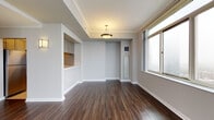 Located at 1 City Place in White Plains, NY, this single-floor residence offers a thoughtfully designed layout with clean, modern finishes throughout. The living area makes a strong first impression with rich, dark hardwood flooring, crown molding, and a decorative pendant light fixture. A pass-through opening connects to the kitchen area, lending an open, communicative feel between spaces, while large windows allow natural light to fill the room.

The kitchen is efficiently laid out in a galley configuration, featuring wood-toned cabinetry, light countertops, a stainless steel sink, and a full-size refrigerator. Light tile flooring contrasts neatly with the darker hardwood found in the living and sleeping areas.

The bedrooms are generously proportioned, each featuring the same warm hardwood flooring and large windows that frame views of the surrounding White Plains cityscape. Neutral gray walls provide a versatile backdrop, and the rooms benefit from ample natural light.

The bathroom is finished with warm golden marble-style tile on both the floors and tub surround, creating an elegant and cohesive aesthetic. A classic pedestal sink, oval mirror, and soaking tub with a curved shower rod complete the well-appointed space. Overall, the residence combines contemporary practicality with refined design details.