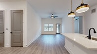 This well-appointed single-story home offers a thoughtfully designed layout across three bedrooms, two bathrooms, and dedicated laundry spaces. The open-concept living and kitchen area serves as the heart of the home, featuring light gray wood-look flooring, elevated ceilings, and a ceiling fan that enhances the airy feel. Large windows and a glass-paneled exterior door allow abundant natural light to fill the living room. The kitchen stands out with dark wood cabinetry, stainless steel appliances, a built-in wine rack, and a crisp white countertop peninsula illuminated by two stylish brass-and-black pendant lights. The spacious primary bedroom benefits from its own ceiling fan and walk-in closet equipped with wire shelving systems for ample storage. Additional bedrooms are bright and well-sized, each with large windows and consistent light wood flooring. The bathrooms are finished in a clean, neutral palette, with one featuring a tub-shower combination with tiled surround and matte black hardware accents. A dedicated laundry area includes a full-size washer and dryer. Three closets throughout the home provide generous storage options, completing this functional and modern living space.