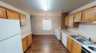 Located at 388 Rue de Gabriel St in Natchitoches, Louisiana, this two-story home offers a practical and well-organized layout across both levels. The kitchen is a standout feature, lined with warm honey-toned oak cabinetry offering generous upper and lower storage. It is equipped with a double-basin sink, an electric range with a ventilation hood, a dishwasher, and light-colored countertops. Rich, dark hardwood-style flooring runs throughout the kitchen and main living areas, adding warmth and visual continuity. Notably, in-unit washer and dryer hookups are conveniently located just off the kitchen, adding everyday functionality. A pendant chandelier provides ambient lighting over the adjacent dining or living area, which is brightened by a window with blinds. The staircase, as seen in the floor plan overview, connects the two levels with a clean, open design. The upper floor hosts multiple bedrooms finished with plush neutral carpeting and bright windows fitted with blinds that allow for natural light. The bathrooms are clean and functional, featuring a tub-shower combination, a single vanity with a mirror, and hardwood-style flooring. The overall aesthetic is neutral and move-in ready throughout.