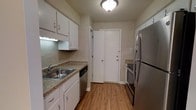 This single-floor 1-bedroom, 1-bathroom residence offers a practical and well-appointed layout designed for comfortable everyday living. The kitchen is a standout feature, showcasing white cabinetry that extends to the ceiling for ample storage, complemented by granite-style countertops and a stainless steel sink. Stainless steel appliances — including a refrigerator, range, and dishwasher — lend the kitchen a modern, cohesive aesthetic. Warm-toned hardwood-style flooring runs throughout, adding a sense of continuity and warmth to the space. The kitchen's galley-style configuration makes efficient use of the available space, with clearly defined work zones along both sides. A doorway at the end of the kitchen leads further into the residence, providing a natural flow between the cooking area and the remaining rooms. Neutral wall tones and flush ceiling lighting keep the atmosphere clean and bright. The overall design balances classic and contemporary elements, making it a welcoming and functional home.
