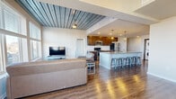 This well-appointed 4-bedroom, 4-bathroom single-floor unit offers a thoughtfully designed layout ideal for shared living. The open-concept common area is immediately striking, featuring rich hardwood flooring and a distinctive slatted wood ceiling that adds architectural character throughout. Large windows flood the living room with natural light while framing views of the surrounding neighborhood's rooftops and mature trees.

The kitchen is a standout feature, centered around an expansive granite-topped island with seating for multiple occupants. Dark walnut cabinetry, stainless steel appliances — including a refrigerator, range, and microwave — pendant lighting, and a dedicated in-unit stacked washer and dryer round out this highly functional space.

Each of the four bedrooms is carpeted and designed for comfort, with oversized windows that bring in natural light and outdoor views. The bedrooms include built-in storage solutions, and several feature the same distinctive slatted ceiling detail found in the common areas. Each bedroom is paired with its own bathroom, offering enhanced privacy. The bathrooms are finished with granite-top vanities, dark cabinetry, tile flooring, and clean white tub-shower combinations. A dedicated closet provides additional storage. Two hallways connect the rooms efficiently, completing this practical and modern floor plan.